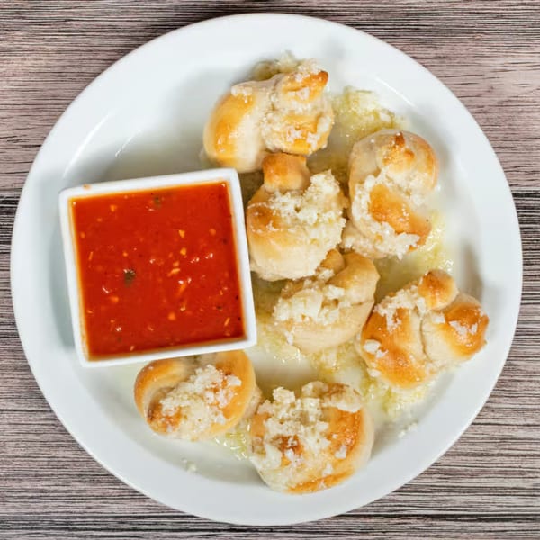 Garlic knots from The Brick Oven Pizza, served with a side of marinara sauce on a white plate.