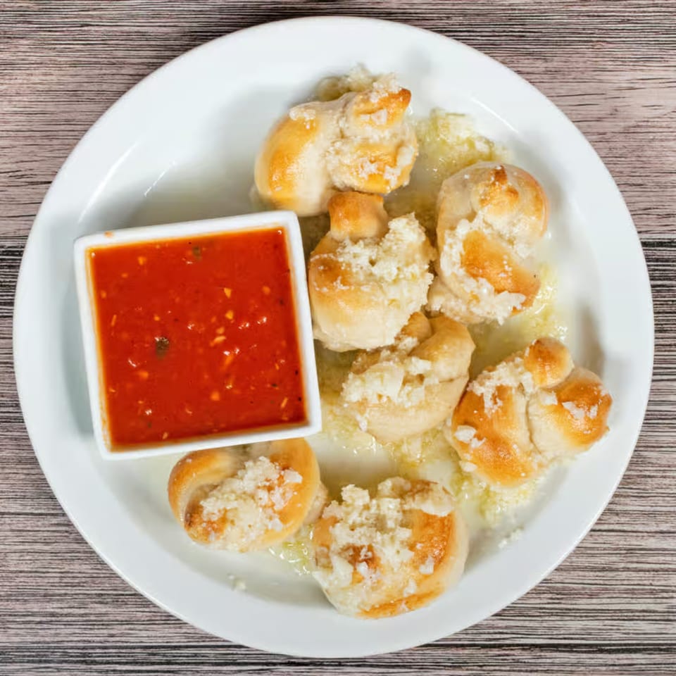 Garlic knots from The Brick Oven Pizza, served with a side of marinara sauce on a white plate.
