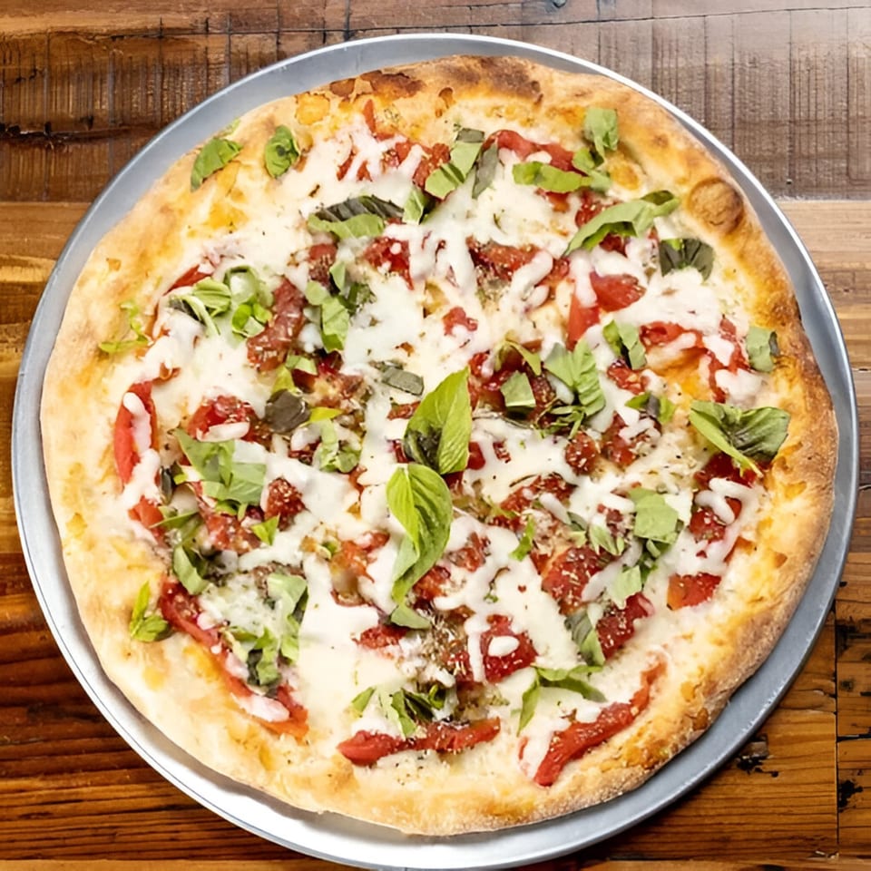 A freshly baked Brick Oven Pizza with melted mozzarella, red sauce, and fresh basil on a wooden table.