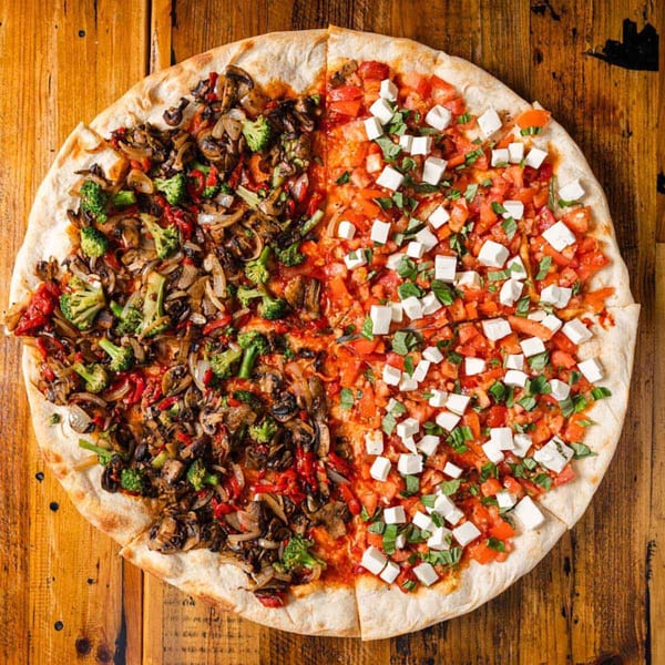 Half vegetable pizza with mushrooms and broccoli, half bruschetta pizza with tomatoes and feta.