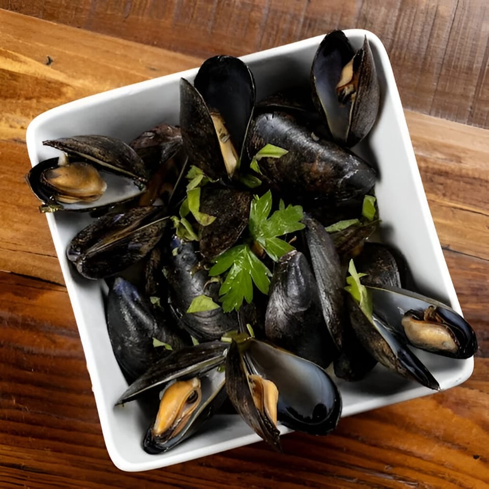 Steamed mussels with fresh parsley in a white rectangular bowl on a wooden table.