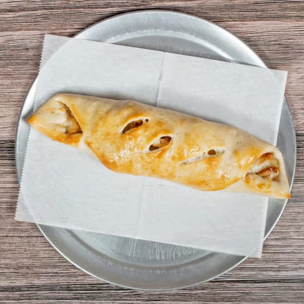 Golden-brown calzone with visible cheese and fillings, served on parchment paper on a metal pizza pan.