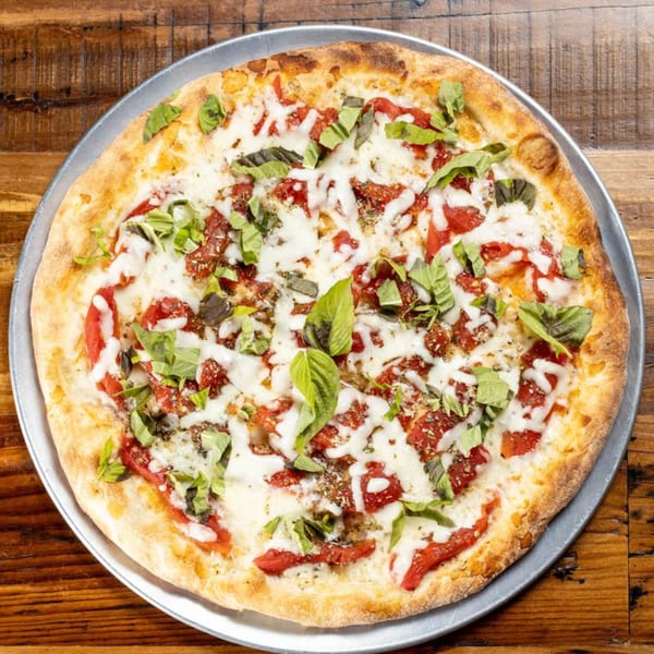 A whole Brick Oven Pizza with melted mozzarella, red sauce, and fresh basil on a wooden table.